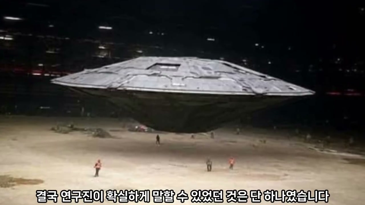 격납고 한가운데 떠 있는 거대한 원반형 비행체와 그 아래 선 작업자들